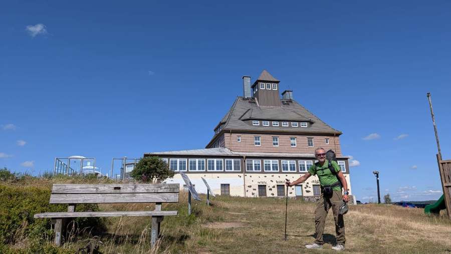 Baude auf dem Schwartenberg mit Aussichtsturm, davor eine Holzbank